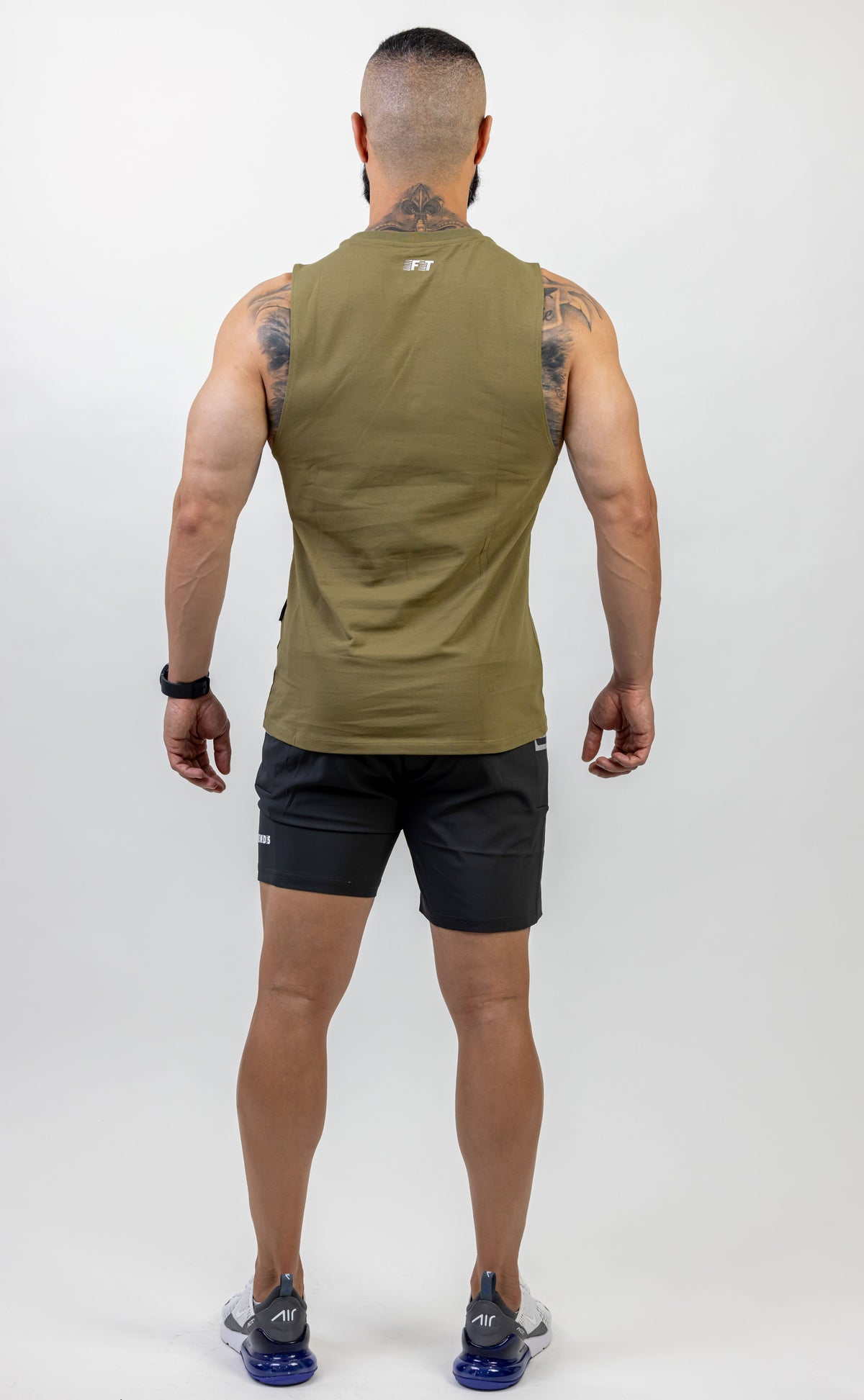 Man wearing an olive green sleeveless shirt and black shorts on a white background