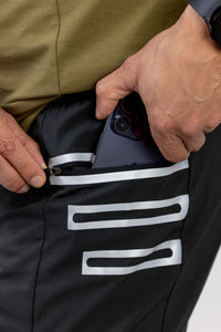 Person putting a phone into a black pocket with white stripes on a green jacket.
