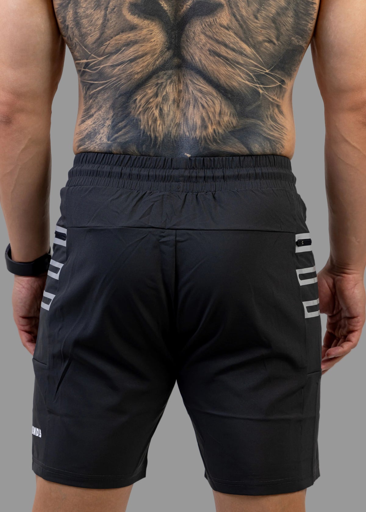 Person wearing black athletic shorts with white stripes on a plain background