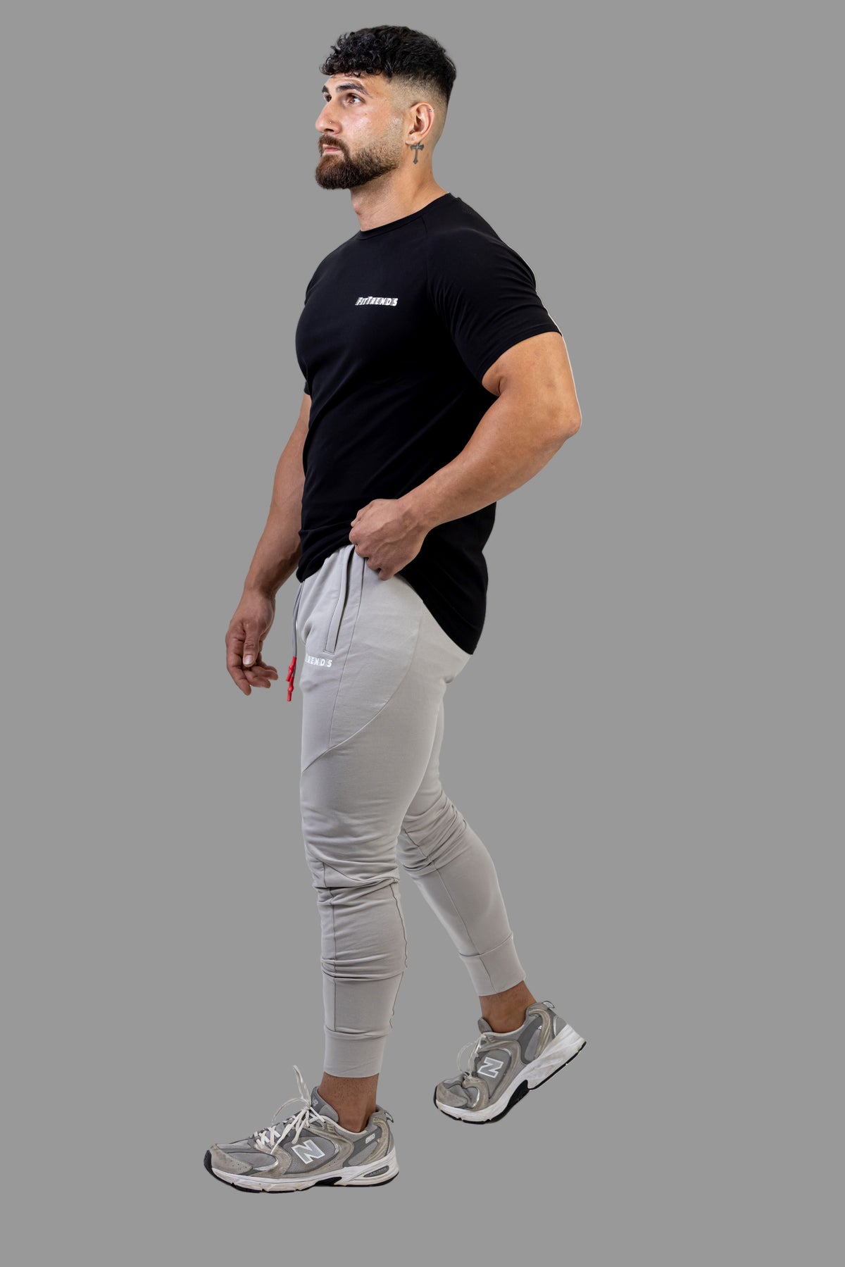 Man wearing a black t-shirt and gray jogger pants on a white background