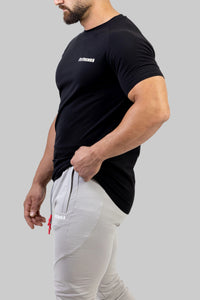 Person wearing a black t-shirt with a logo and light gray pants on a gray background