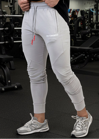 Person wearing light gray jogger pants with a brand logo in a gym setting