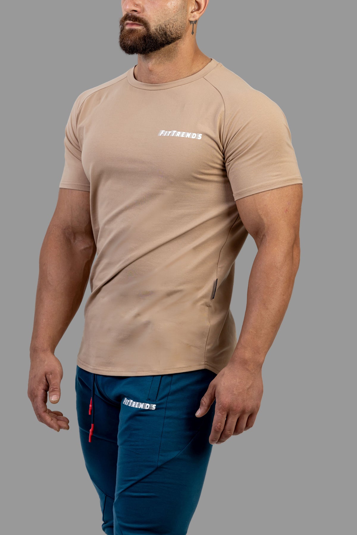 Man wearing a beige athletic shirt and blue shorts with a brand logo on a white background