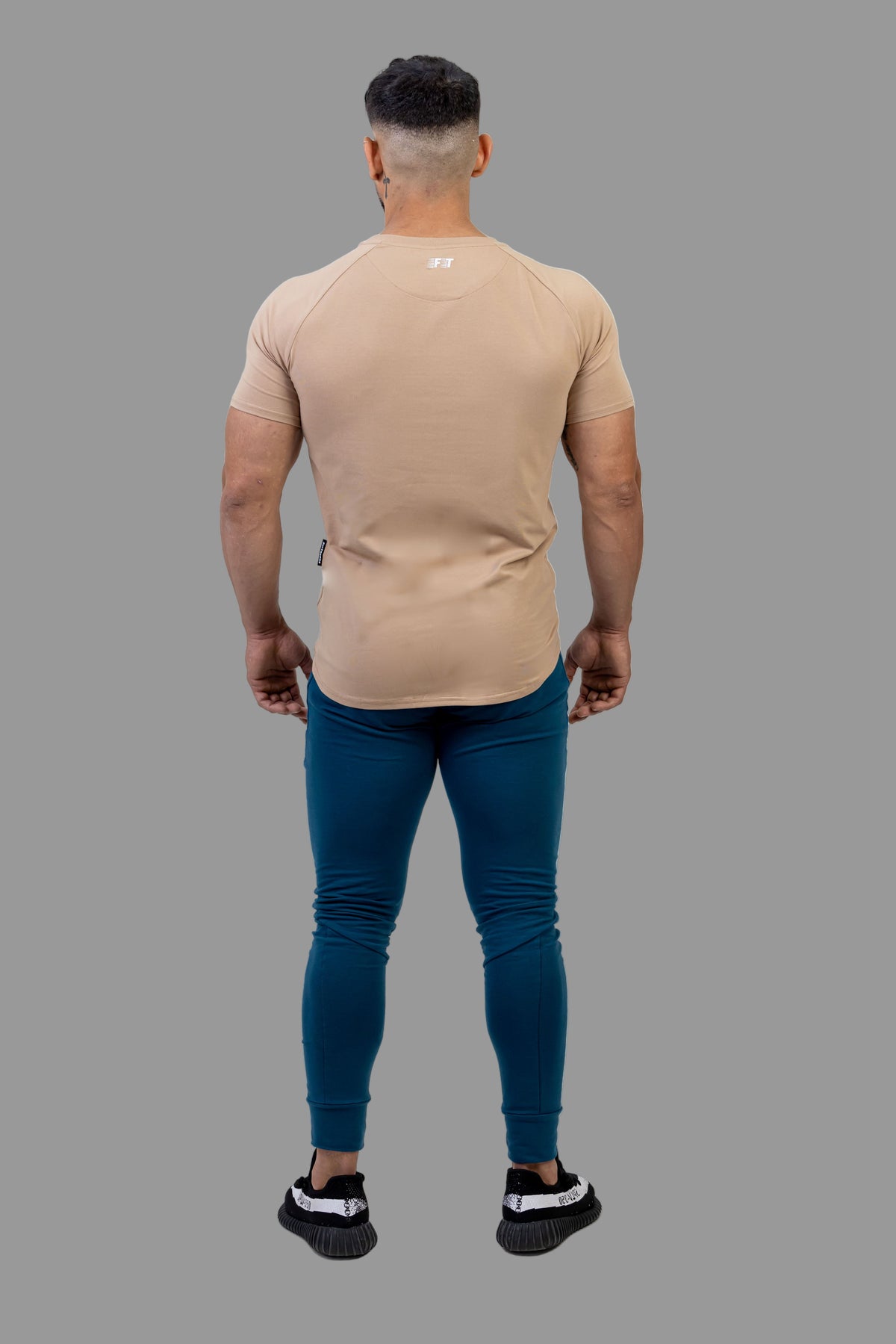 Man wearing a beige t-shirt and blue jeans on a white background