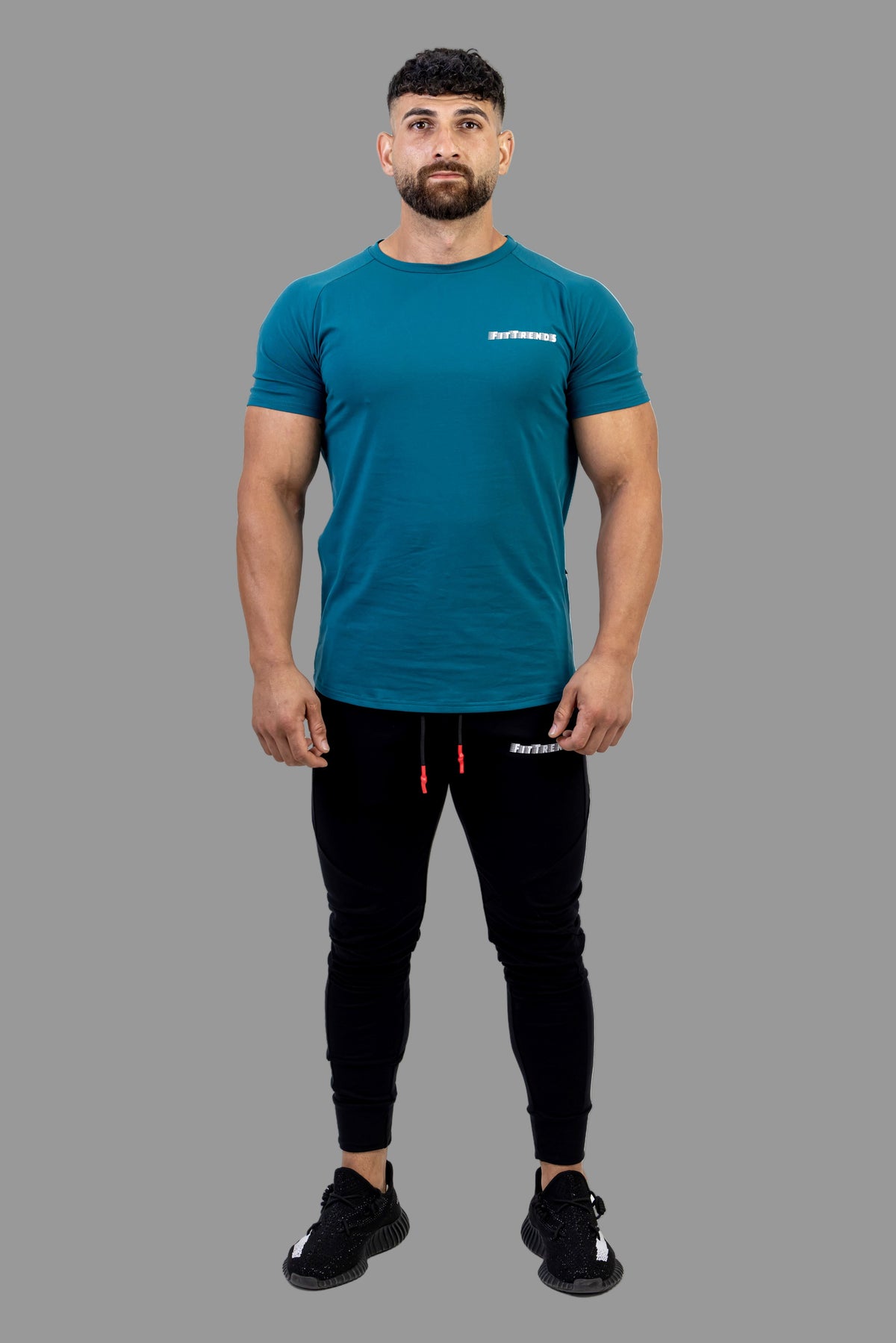 Man wearing a teal t-shirt and black pants on a white background