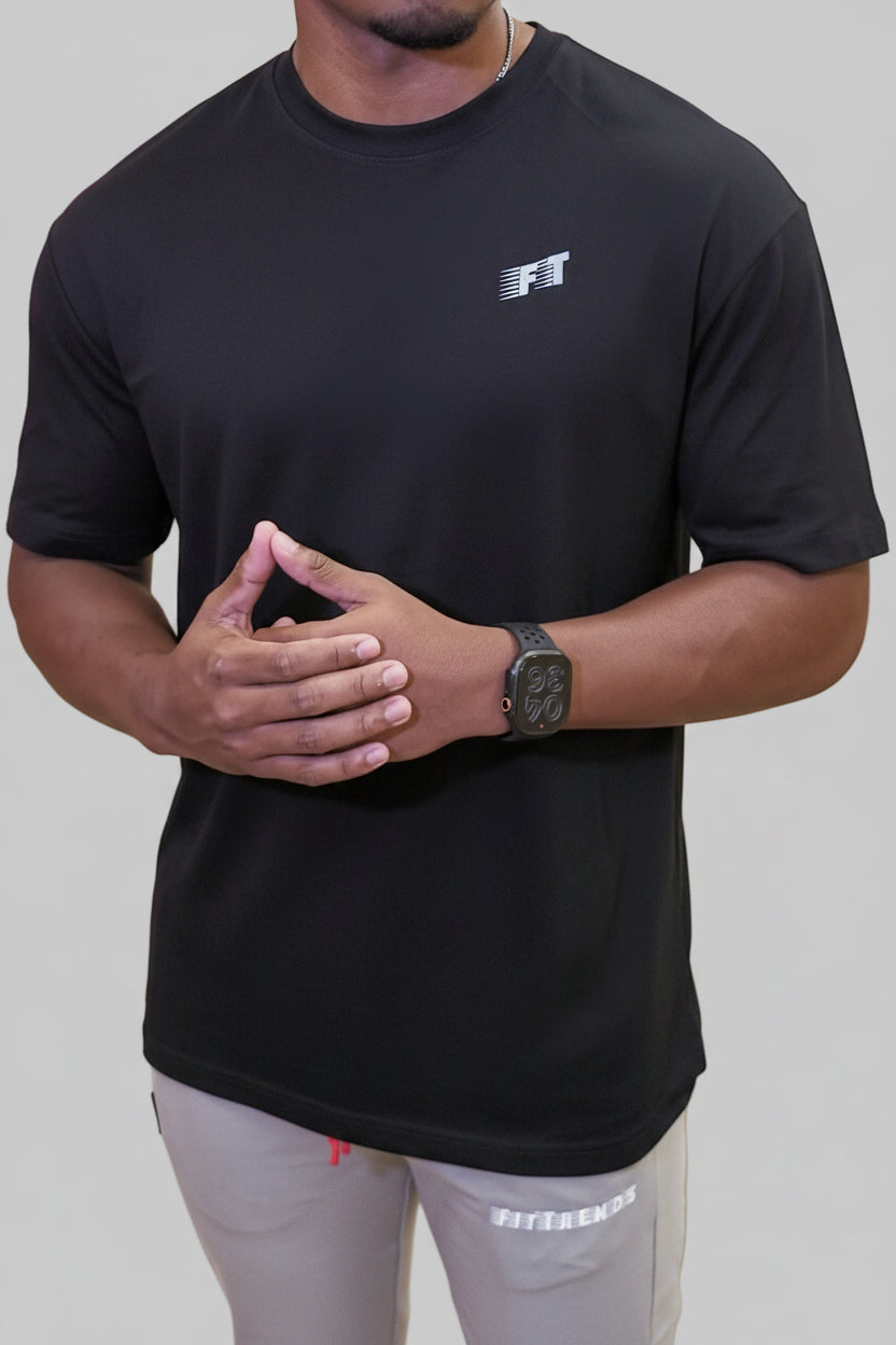 Person wearing a black t-shirt with a logo, standing against a wooden wall.