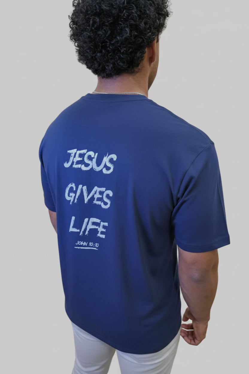 Person wearing a blue t-shirt with 'Jesus Gives Life' text, standing in front of a wall with large pink letters.