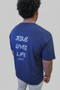 Person wearing a blue t-shirt with 'Jesus Gives Life' text, standing in front of a wall with large pink letters.