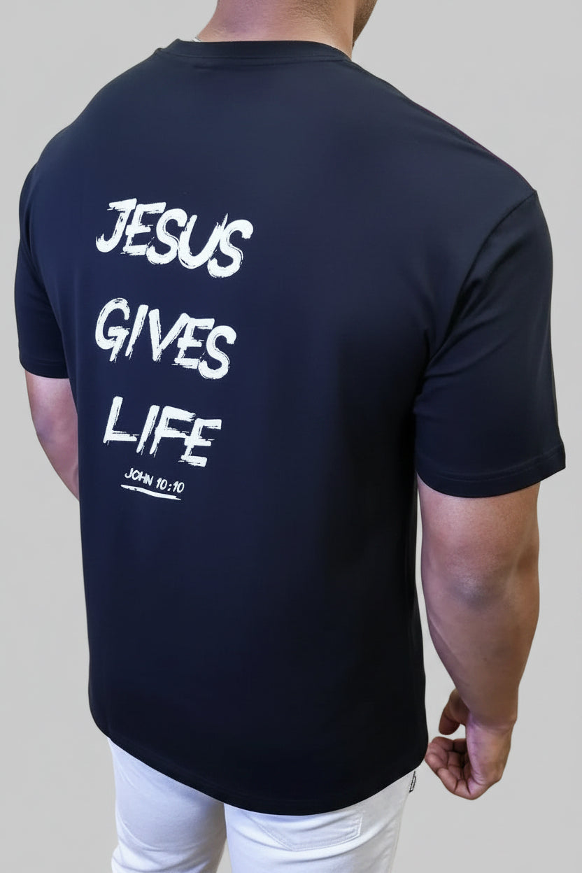 Person wearing a black t-shirt with 'Jesus Gives Life' text, standing in front of a wall with large pink letters.