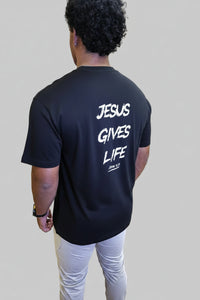 Person wearing a black t-shirt with 'Jesus Gives Life' text, standing in a gym setting.