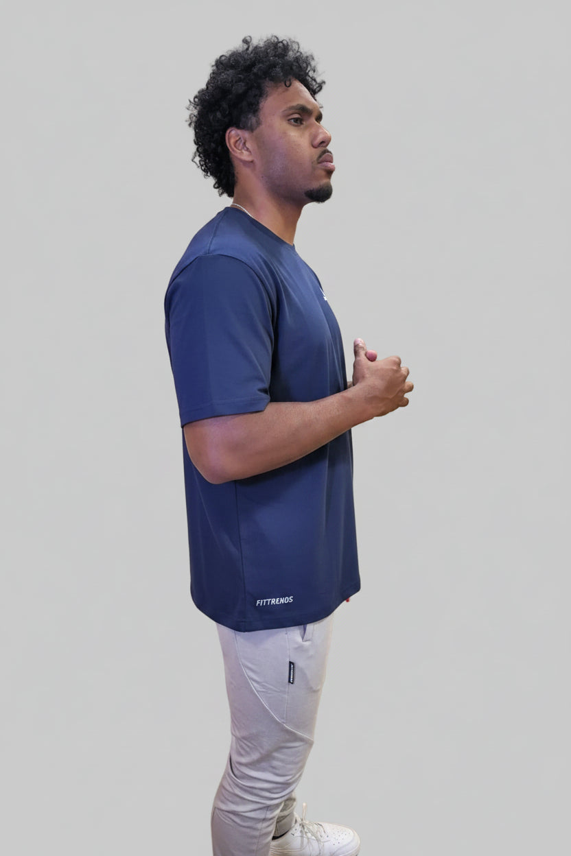 Man in a blue shirt standing in a gym with wooden floor and wall.