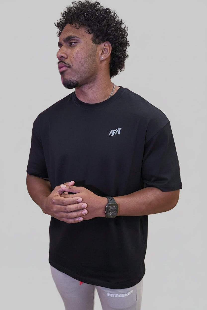 Man wearing a black t-shirt with a logo in front of a pink and purple abstract wall design.