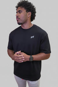 Man wearing a black t-shirt with a logo in front of a pink and purple abstract wall design.