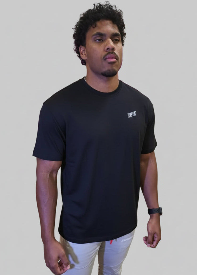 Person wearing a black t-shirt with a logo in front of a wooden wall with large pink letters.