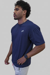 Person wearing a blue t-shirt with a brand logo against a wooden wall with large pink letters.
