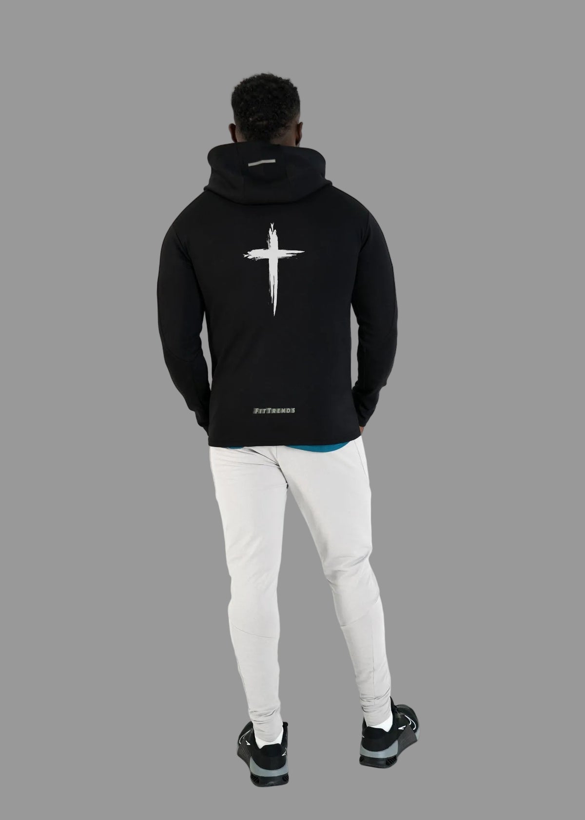 Person wearing a black hoodie with a white cross design on the back, standing against a white background.