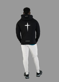 Person wearing a black hoodie with a white cross design on the back, standing against a white background.