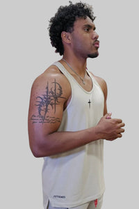 Man wearing a white tank top with visible tattoos on his arm against a gray background