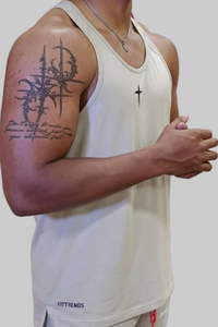 Person wearing a white tank top with visible tattoos on an arm, standing against a plain background.