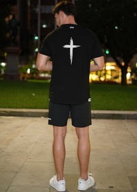 Person wearing a black t-shirt with a white cross design outdoors at night.