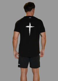Person wearing a black t-shirt with a white cross design on the back, standing outdoors at night.