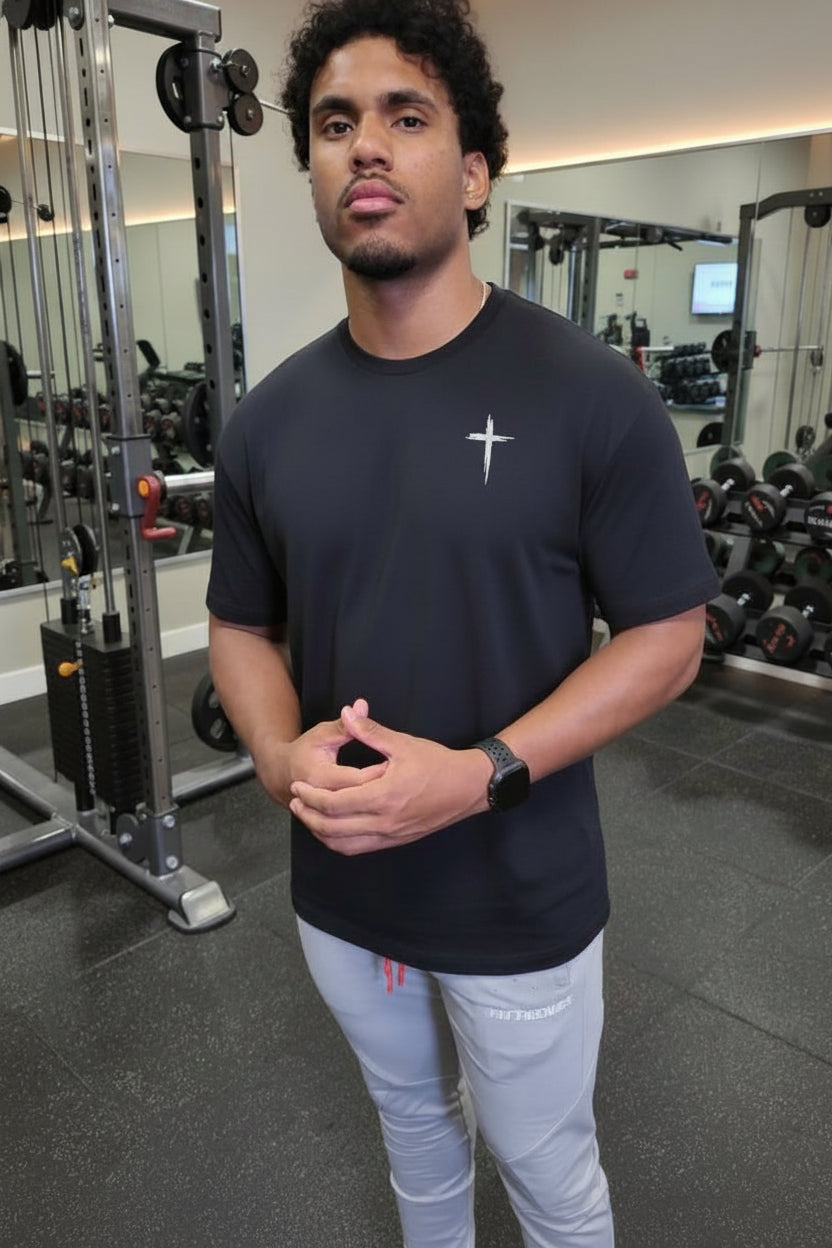 Man in a gym wearing a black t-shirt with a logo and light gray pants.