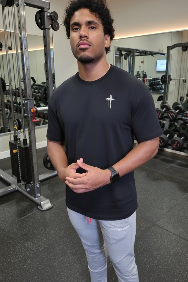 Man in a gym wearing a black t-shirt with a logo and light gray pants.