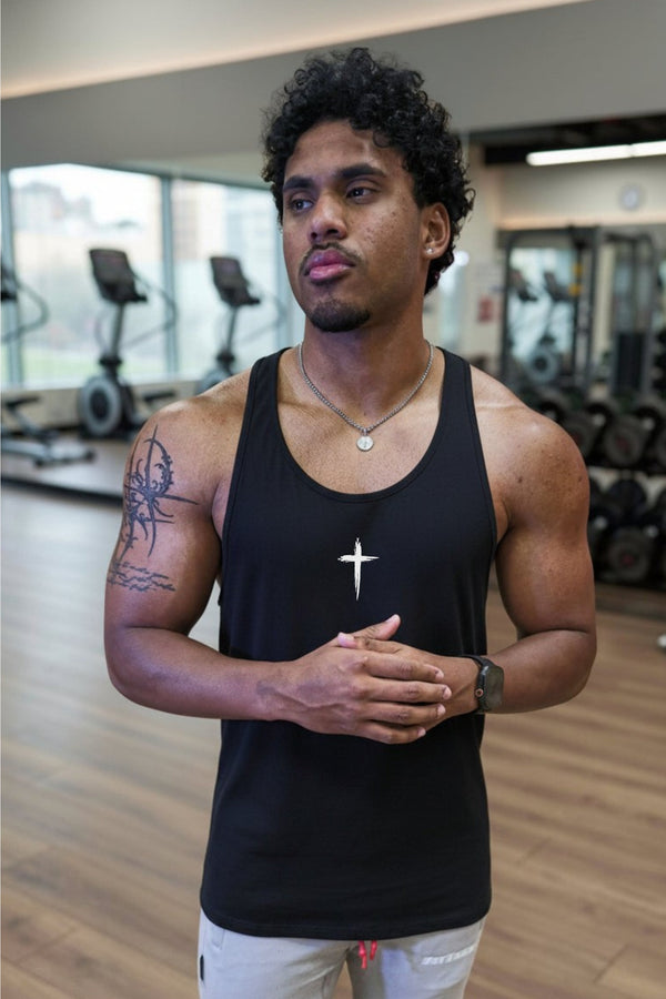 Man in a black tank top standing in a gym with a cross logo