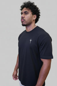 Man wearing a black t-shirt with a logo in front of a wooden wall with pink text.