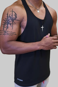 Person wearing a black tank top with visible tattoos on arm, standing against a plain background