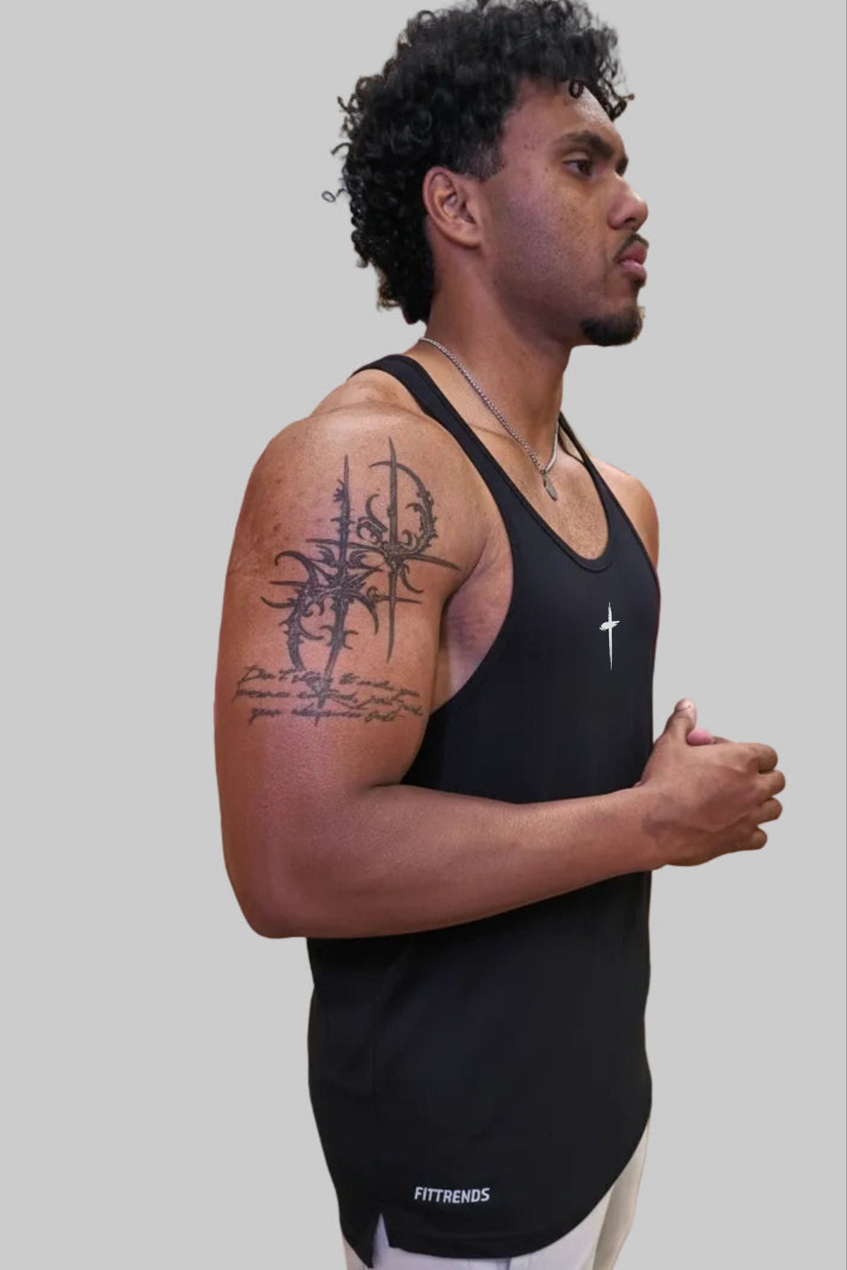 Man wearing a black tank top with visible tattoos on a plain background