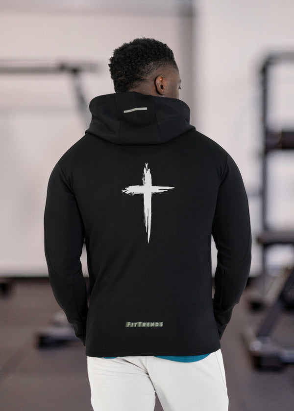 Person wearing a black hoodie with a white cross design on the back, standing in an indoor setting.
