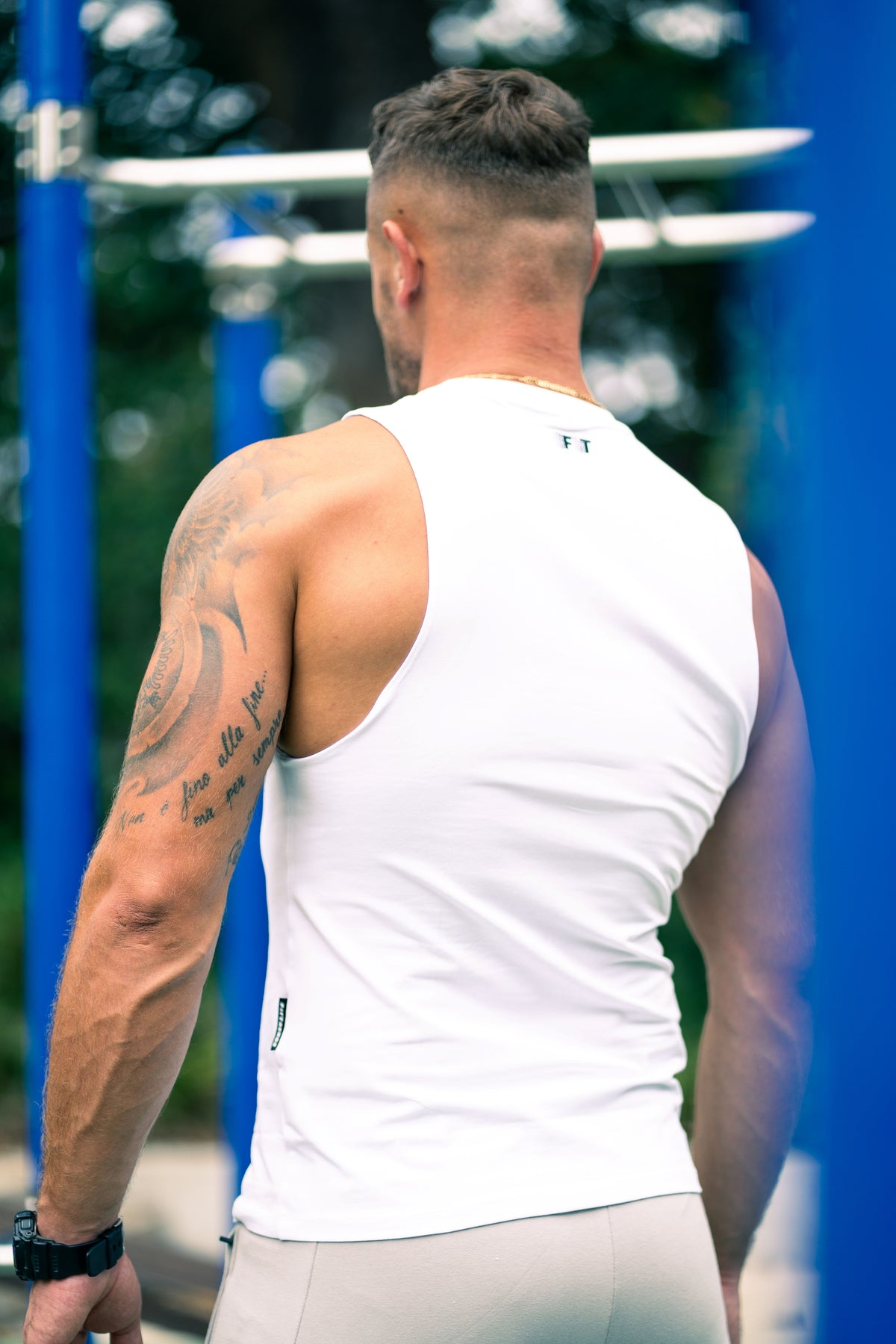 Man wearing a white tank top outdoors with blue and green background