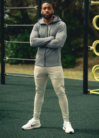 Man wearing a gray hoodie and light-colored pants standing on a playground.
