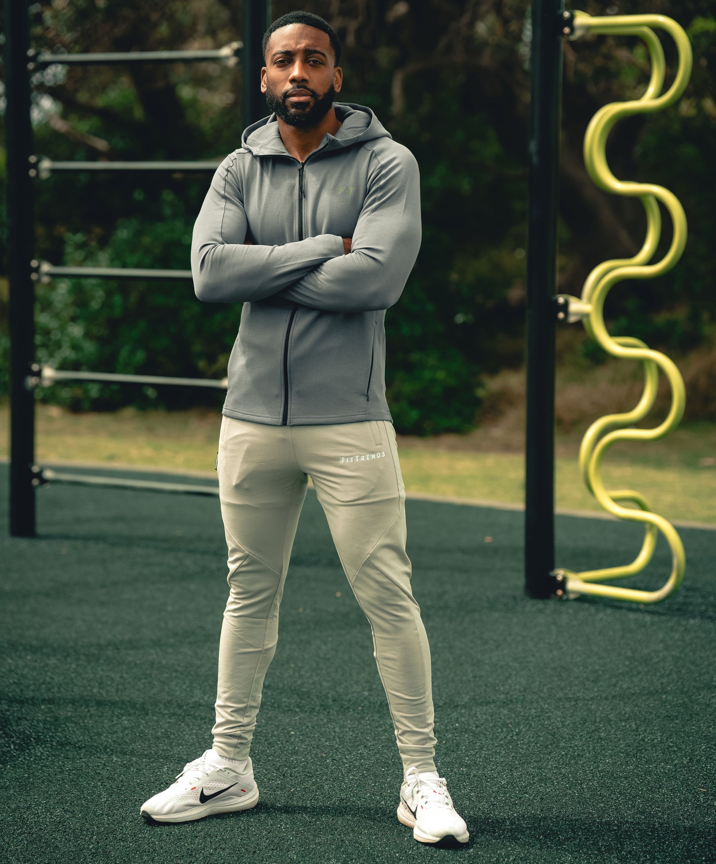 Man wearing a gray hoodie and light-colored pants standing on a playground.