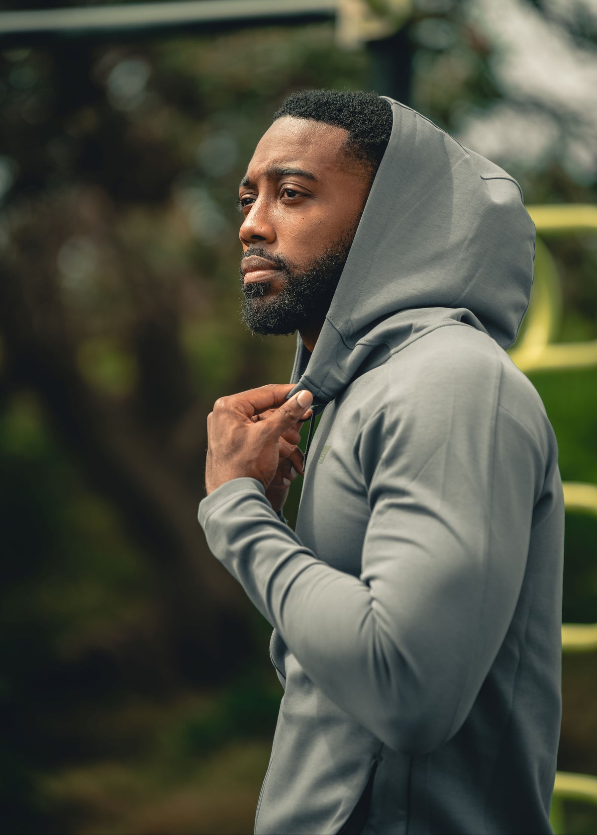 Man wearing a gray hoodie outdoors with a blurred natural background