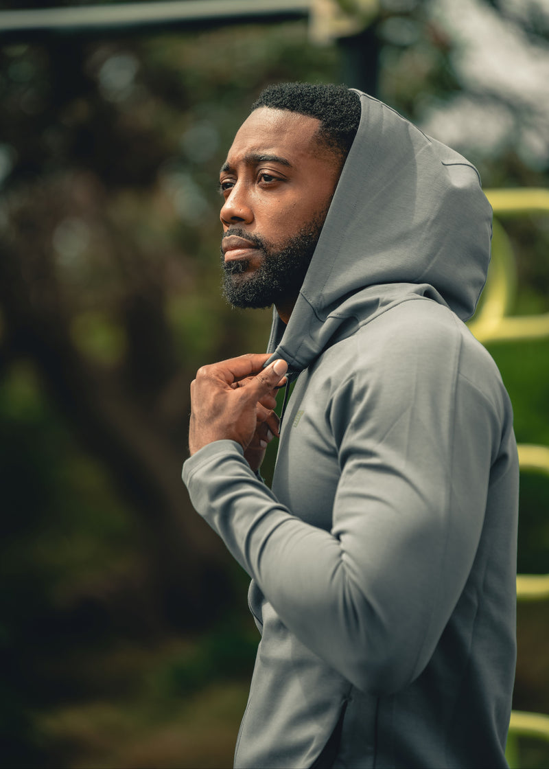 Man wearing a gray hoodie outdoors with a blurred natural background