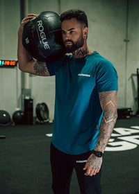 Man holding a Rogue fitness ball in a gym setting