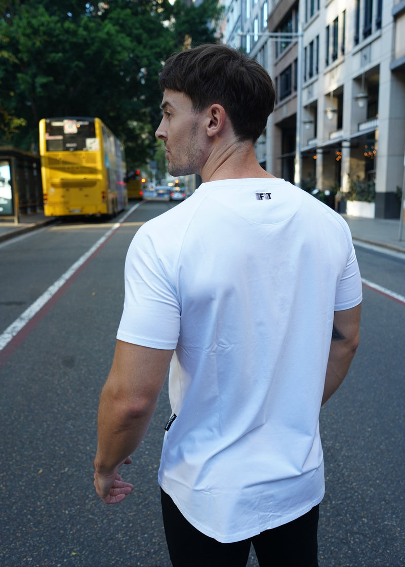 Man in a white shirt standing on a street with buildings and trees in the background