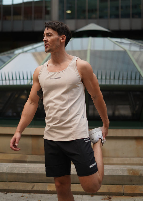 Man in a beige tank top and black shorts standing on a reflective surface with a cityscape background