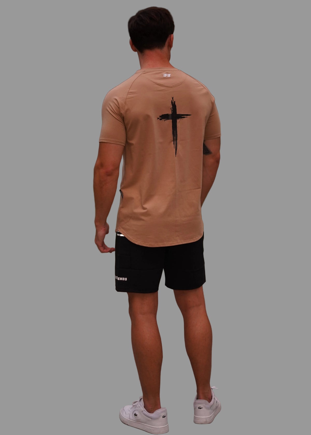 Man walking on a sidewalk with a cross design on his beige t-shirt