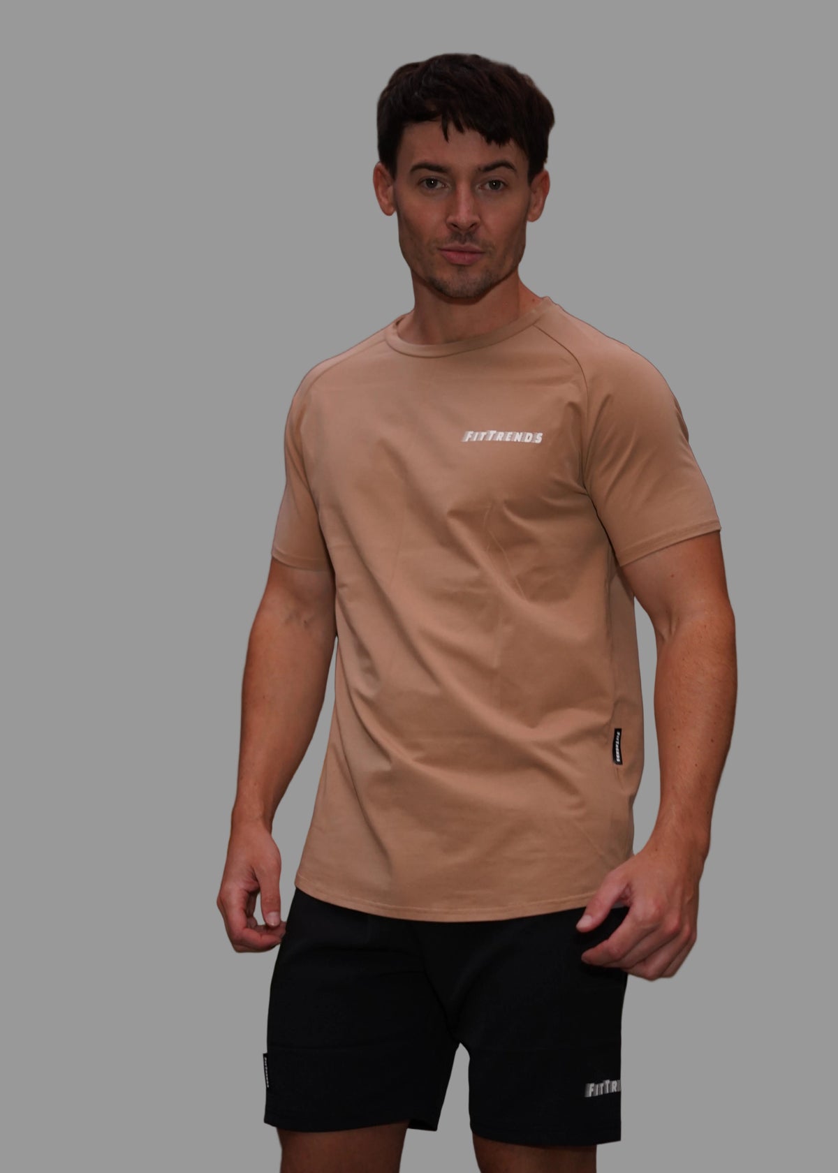 Man wearing a beige t-shirt with a logo, standing outdoors with blurred background
