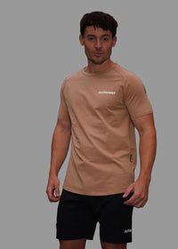 Man wearing a beige t-shirt with a logo, standing outdoors with blurred background