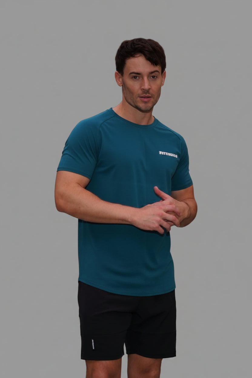 Man in blue t-shirt and black shorts standing on a sidewalk with buildings and trees in the background