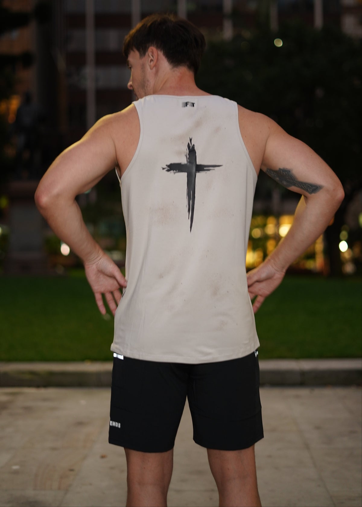 Person wearing a white tank top with a black design outdoors at night.