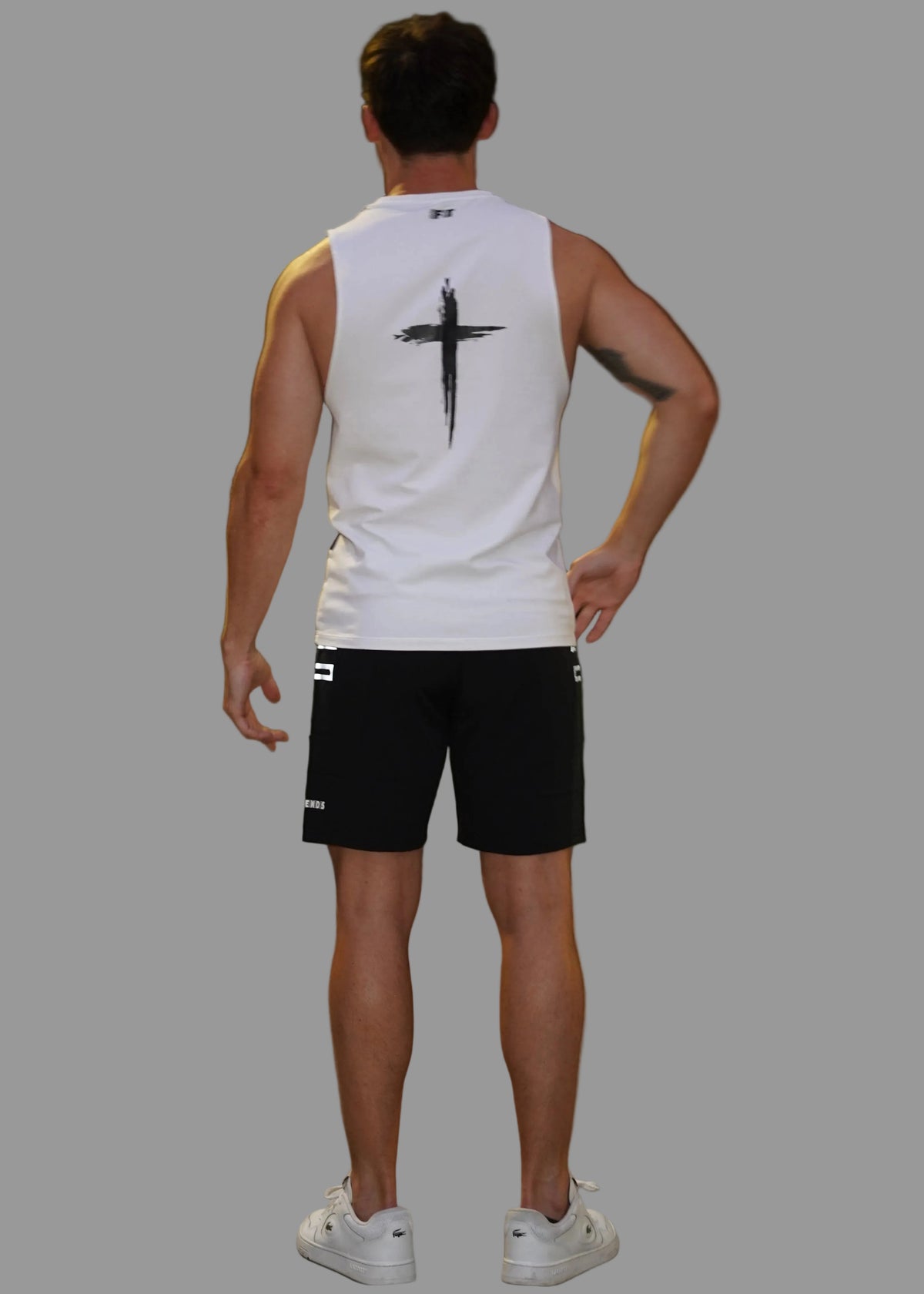 Person wearing a white tank top with a black cross design in an urban setting at night.