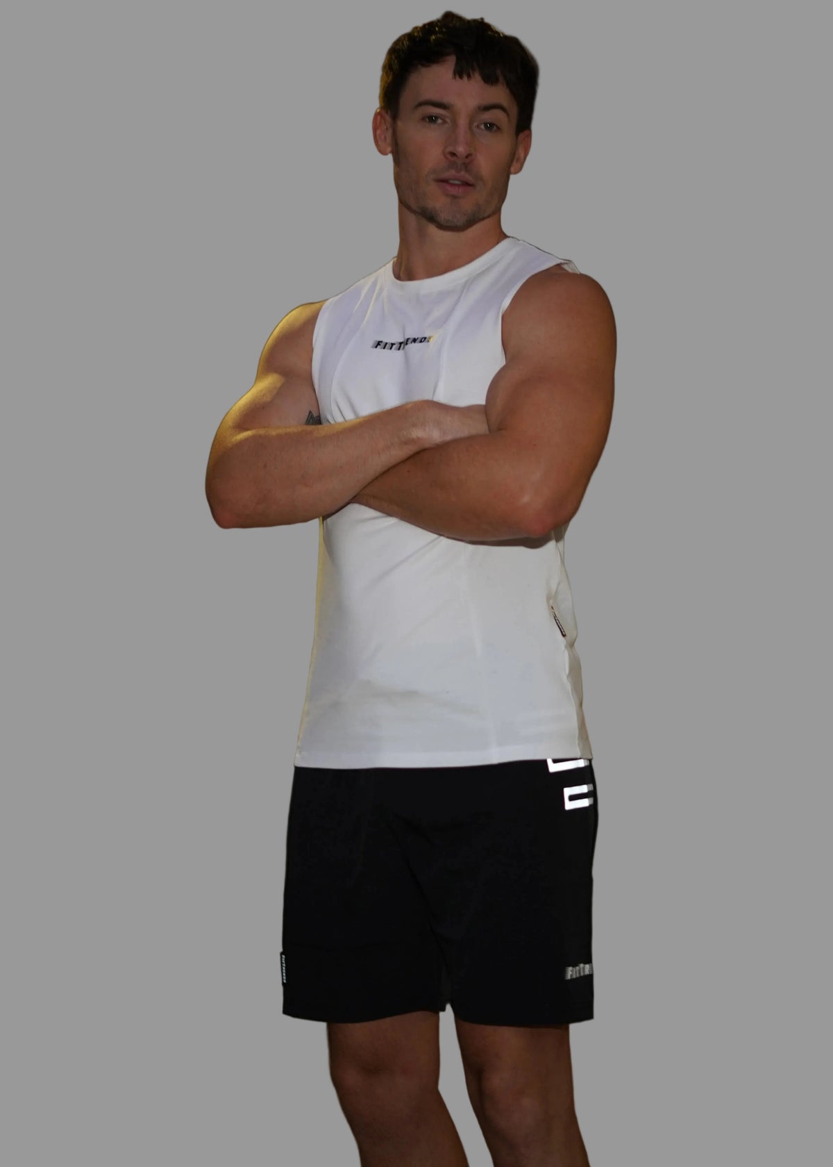 Man wearing a white sleeveless shirt and black shorts standing in an urban night setting.