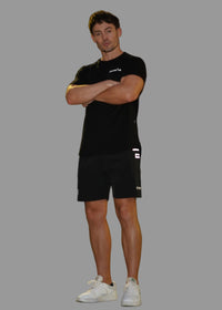Person wearing a black outfit with white shoes standing on a sidewalk at night.