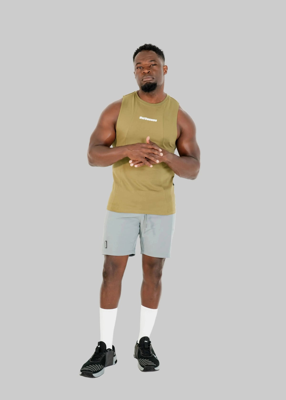 Man wearing a green tank top and gray shorts on a white background