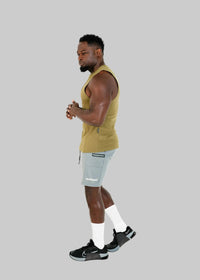 Man wearing a mustard yellow sleeveless shirt and gray shorts on a white background